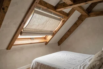 Rideau thermique installé sur une fenêtre de toit Velux dans des combles aménagés avec poutres apparentes