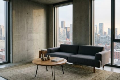 Salon contemporain minimaliste avec canapé gris anthracite, table basse en chêne et tapis en laine beige dans un appartement moderne aux murs en béton